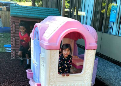 Preschool kids playing in outdoor princess and log cabin playhouses.